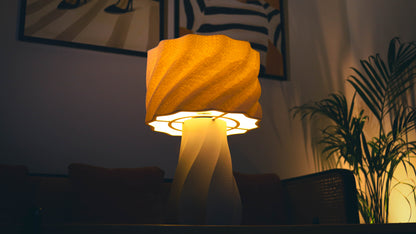 Aurelia Lamp glowing warmly on wooden table beside indoor plant