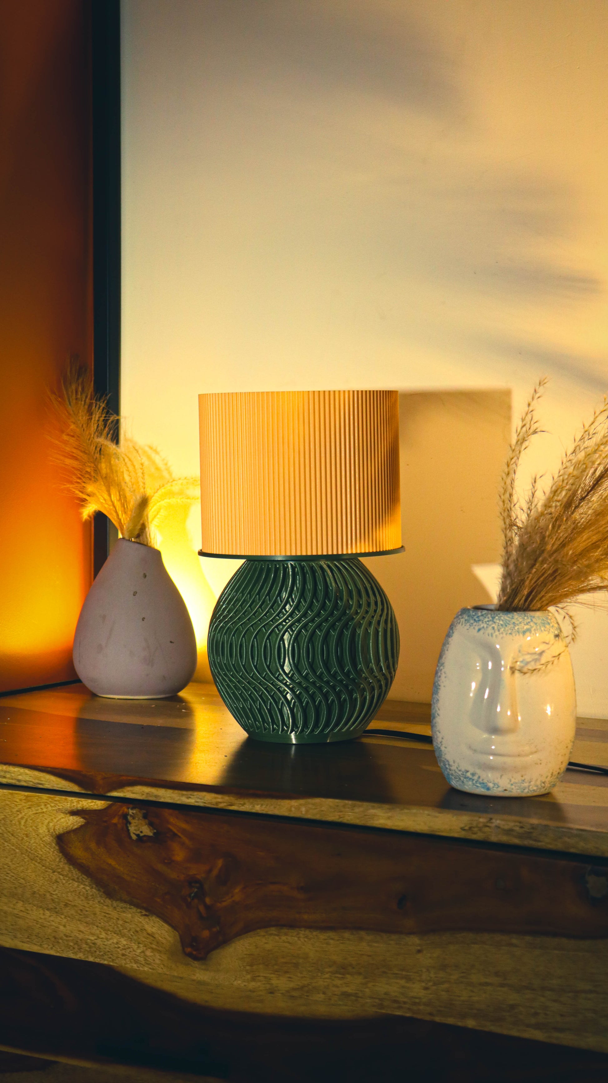 Decorative table setting with a green textured lamp, white vase, and small plant on a wooden surface.