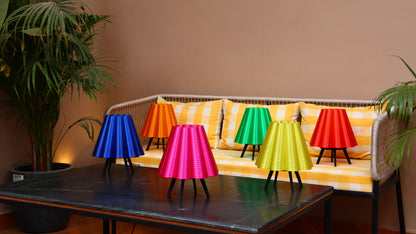 Five pleated tripod lamps in blue, orange, pink, green, and red on striped sofa