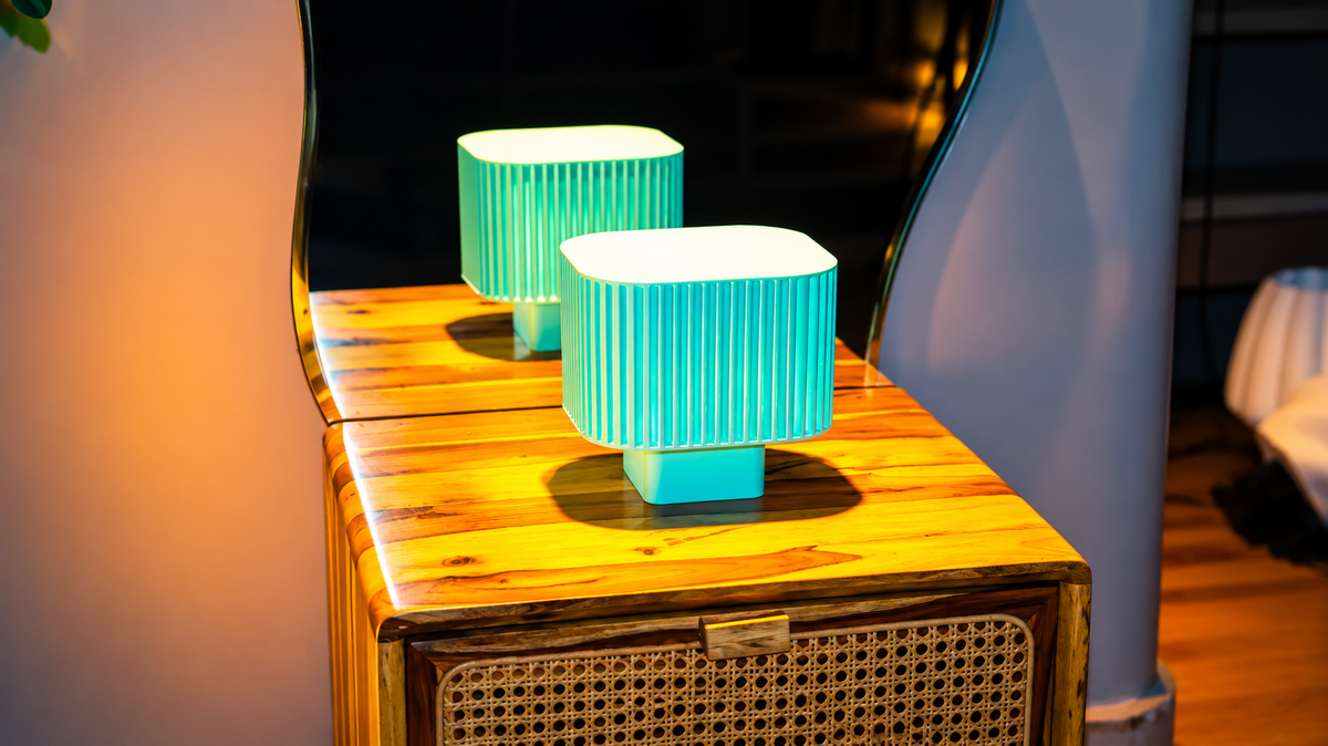 Modern teal ribbed table lamp on a wooden surface with a blurred background