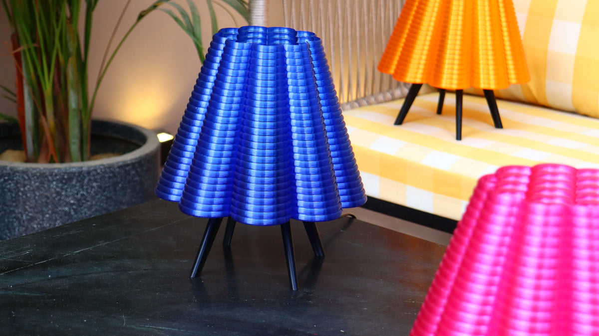 Pleated cone-shade tripod lamp in blue with orange and pink lamps in background